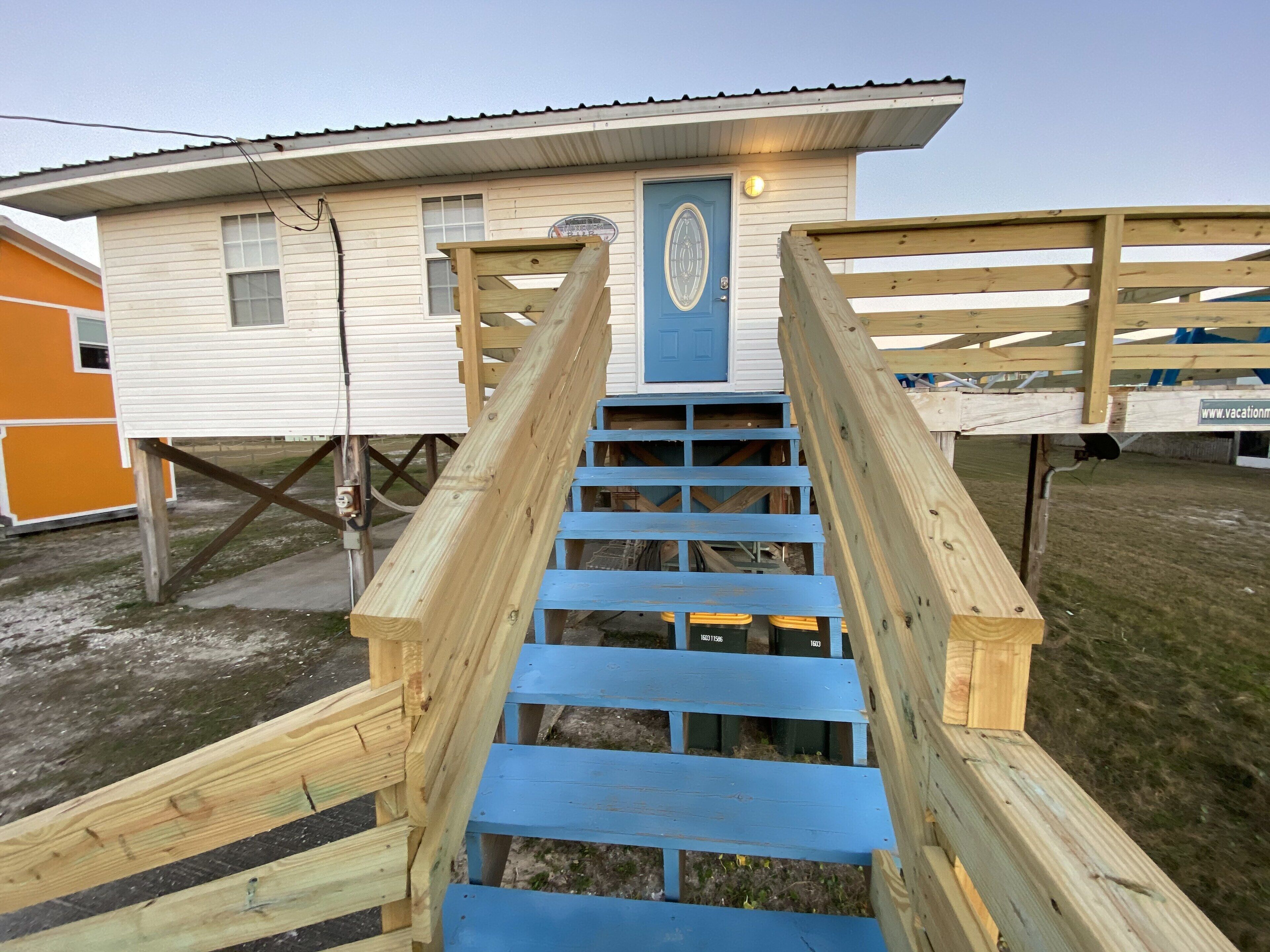 A wooden staircase leading to a house with a blue door.