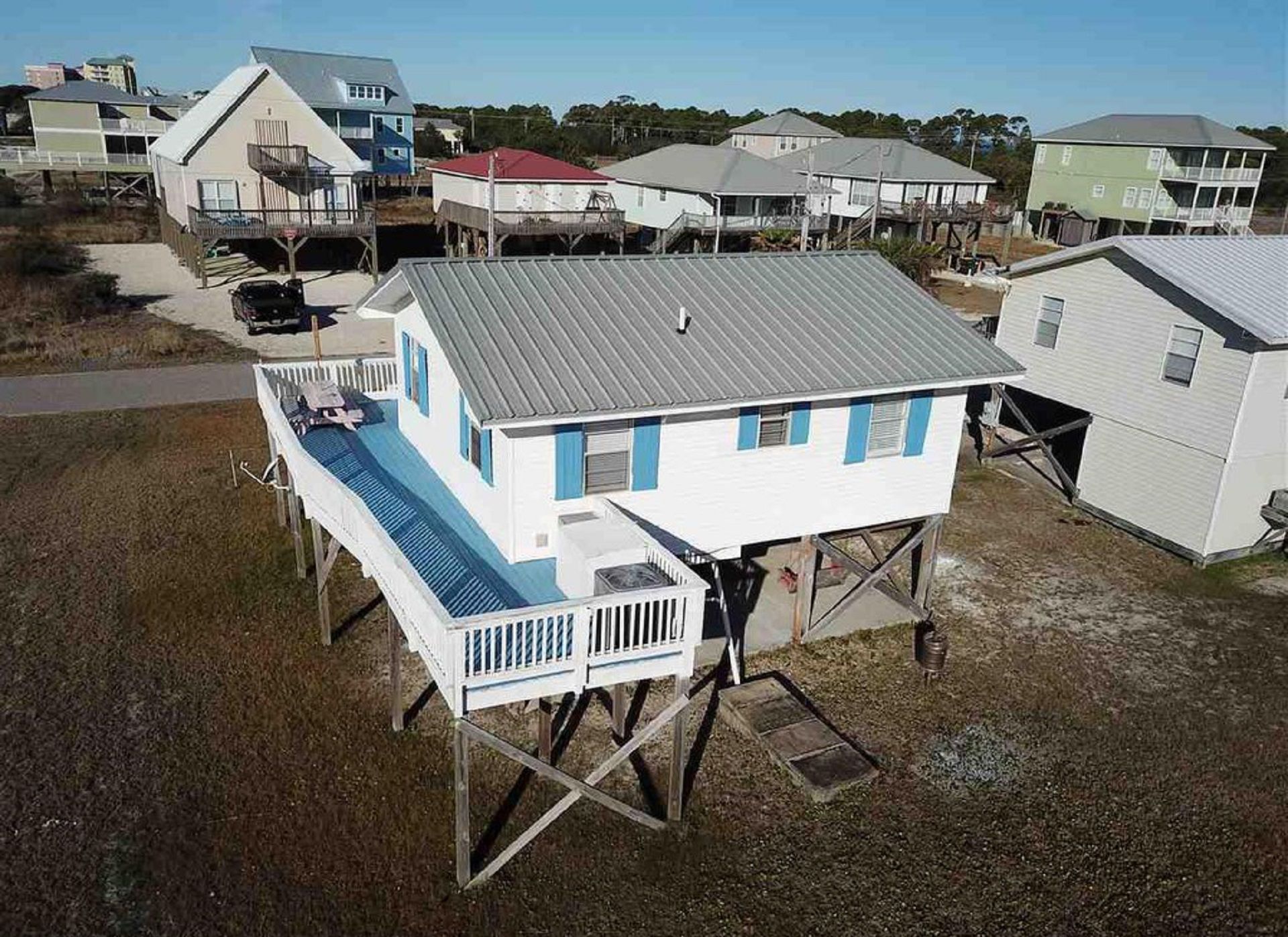A house with a raised deck and a metal roof, surrounded by other houses.