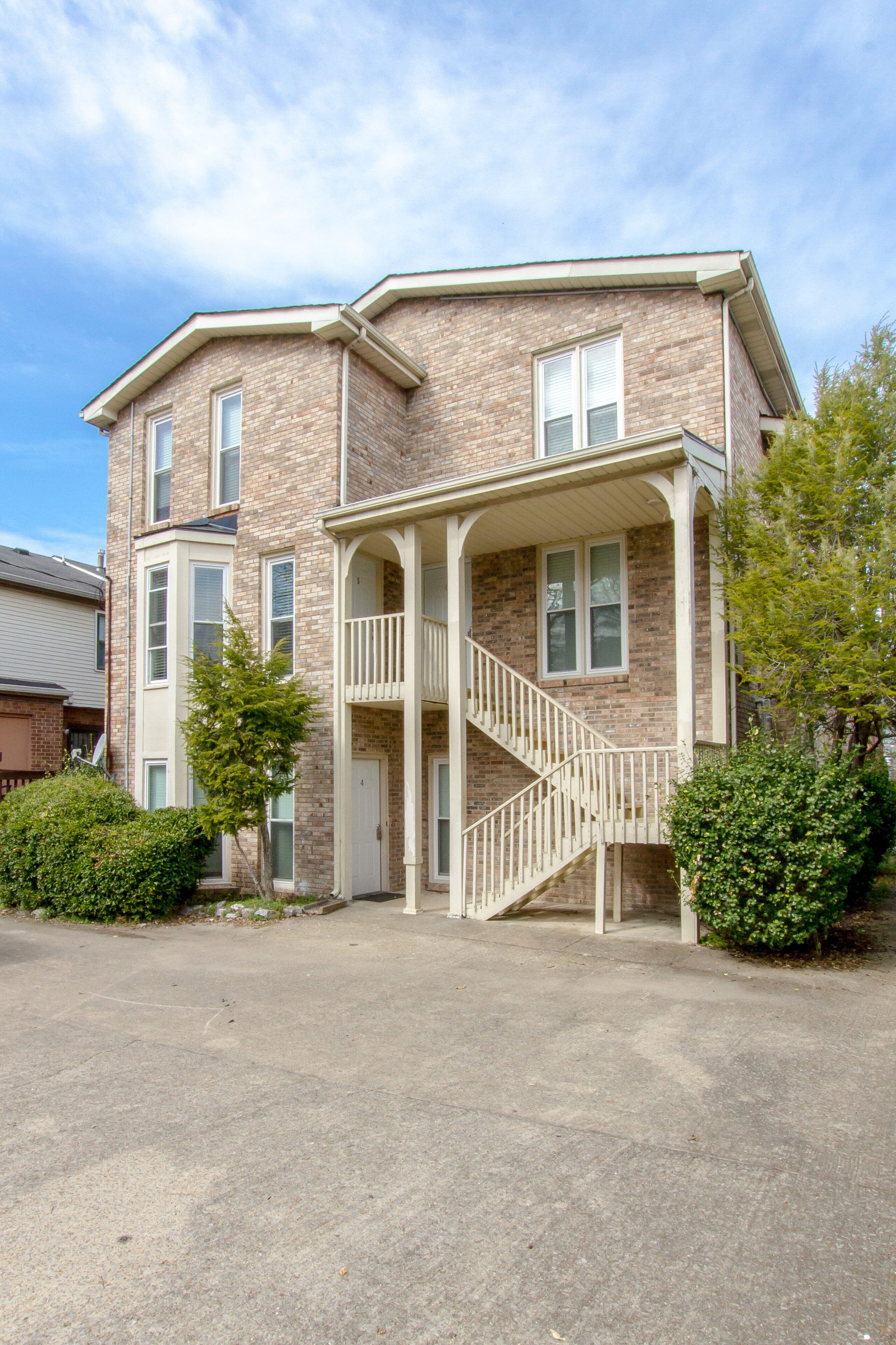 A two-story brick building with a central staircase, a covered porch, and a small front yard with a tree.