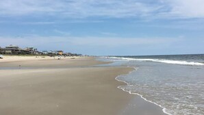 Ein Strand mit sandigem Ufer, einigen Gebäuden im Hintergrund und einem klaren Himmel.