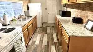 A kitchen with granite countertops, wooden cabinets, a white refrigerator, a microwave, a toaster, and a stove.