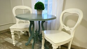 A round table with a glass top and two white upholstered chairs with curved backs.