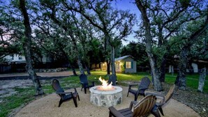 A fire pit surrounded by chairs in a backyard with trees and a house in the background.