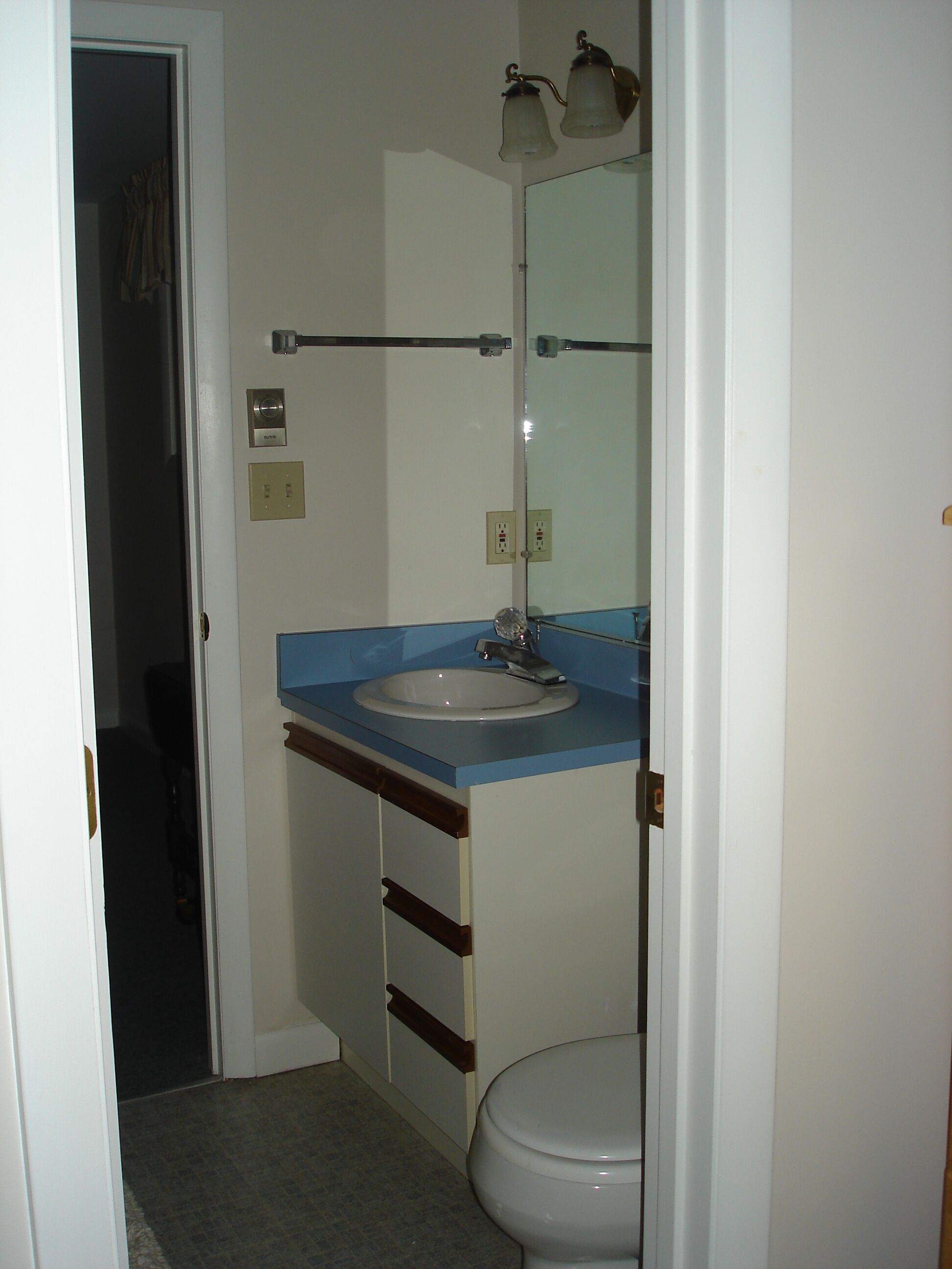 Een badkamer met een wit toilet, een blauwe wastafel en een spiegel erboven.