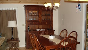 Un comedor con mesa y sillas de madera, un aparador con puertas de cristal, una lámpara y una araña.