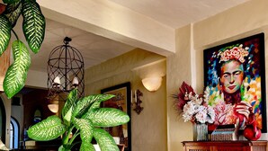 A living room with a wicker sofa, a large green plant, a wooden cabinet, and a colorful painting on the wall. - Los Muertos Beachfront Art Condo with Pano View:  Best Romantic Zone Location (Puerto Vallarta)