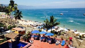 A beach resort with a pool, lounge chairs, umbrellas, and a view of the ocean. - Los Muertos Beachfront Art Condo with Pano View:  Best Romantic Zone Location (Puerto Vallarta)