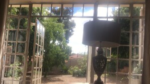 A room with a view through a window, a lamp on a table, and a bed. - Solar powered. Large Garden Apartment, Central & Secure Neighbourhood. (Johannesburg)