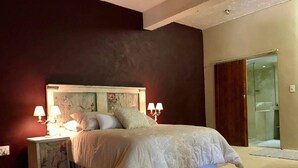 A bedroom with a bed, nightstands, and a nightstand with a floral design. There is a door leading to a bathroom. - Solar powered. Large Garden Apartment, Central & Secure Neighbourhood. (Johannesburg)