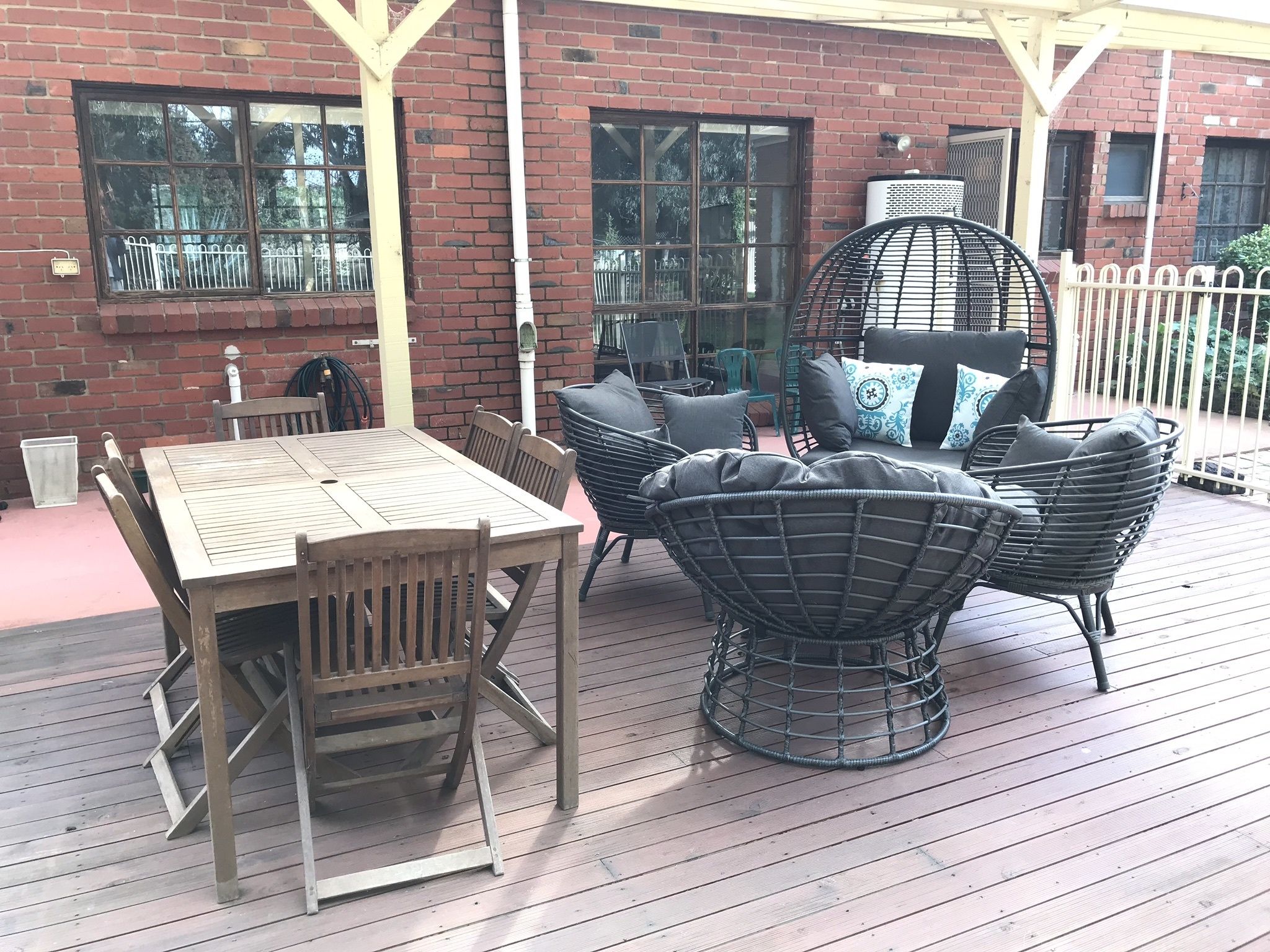 A wooden deck with a table and chairs, a wicker chair, and a cushioned bench with pillows.