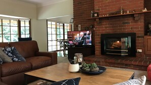 Una sala de estar con chimenea de ladrillo, un sofá de cuero, una mesa de centro con objetos decorativos y un televisor mostrando un noticiero.