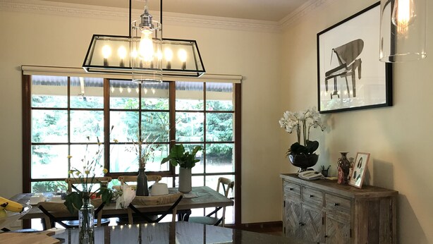 Un comedor con un ventanal grande, una araña y un mueble de madera con un cuadro.