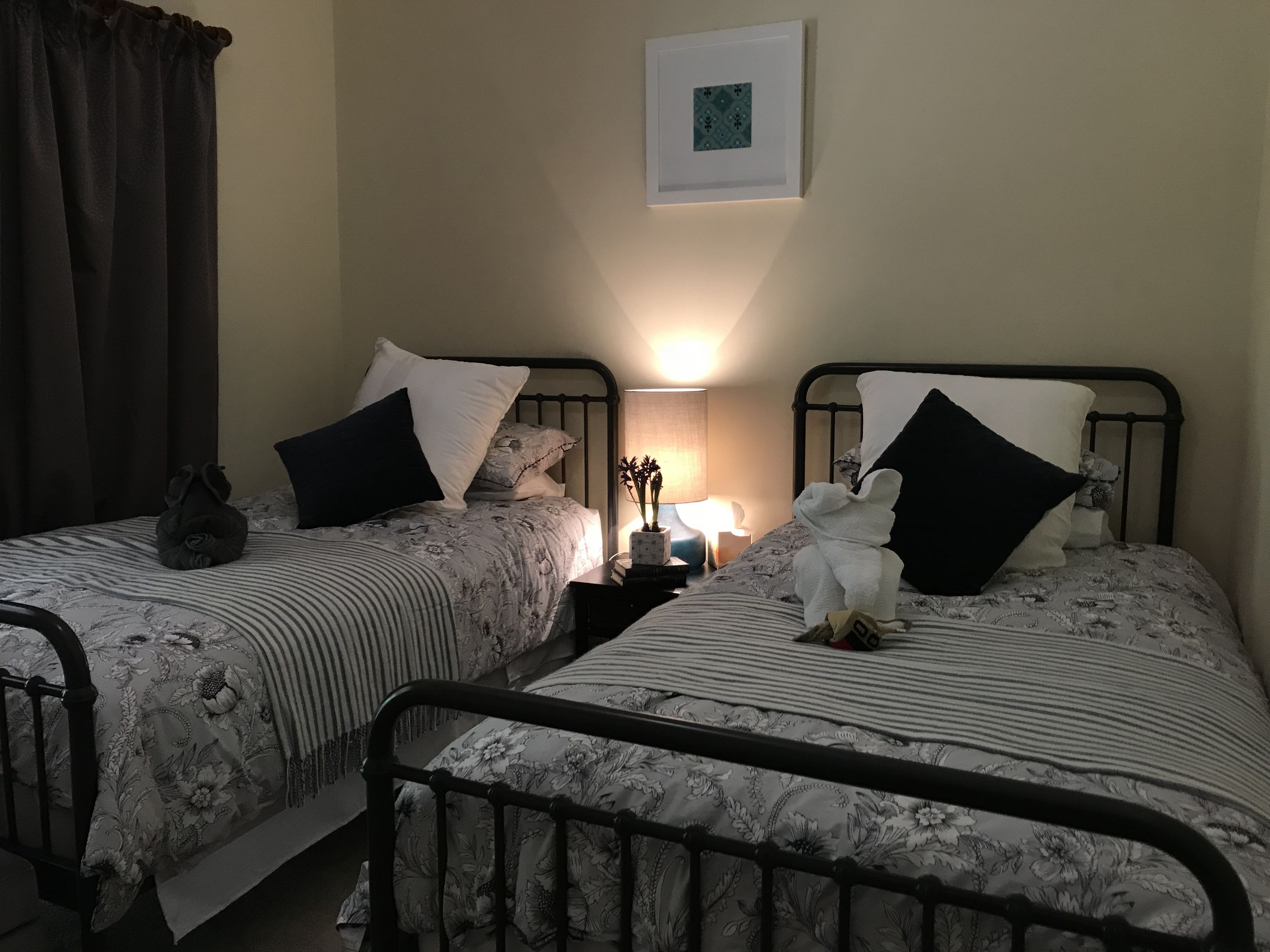 A twin bedroom with two beds, each with floral bedding and black pillows. There is a bedside table with a lamp and a small potted plant.