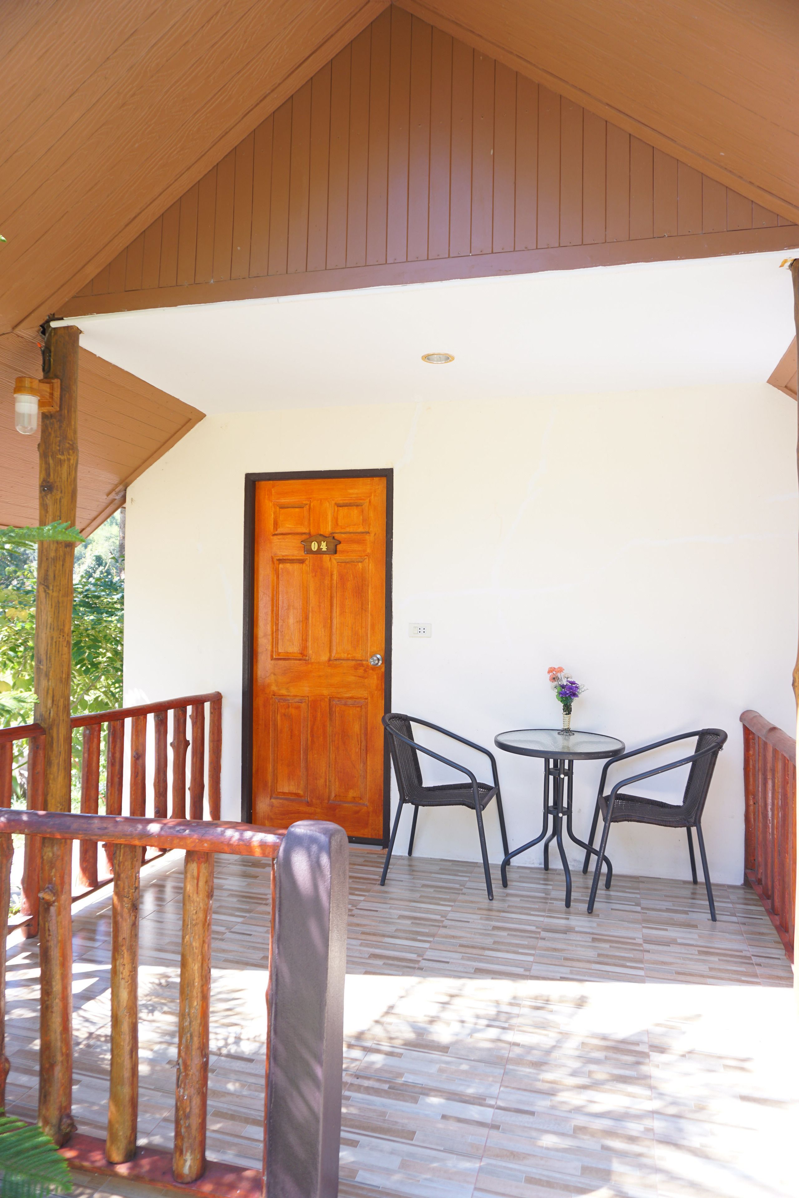 Une terrasse en bois avec une porte, deux chaises et une petite table.