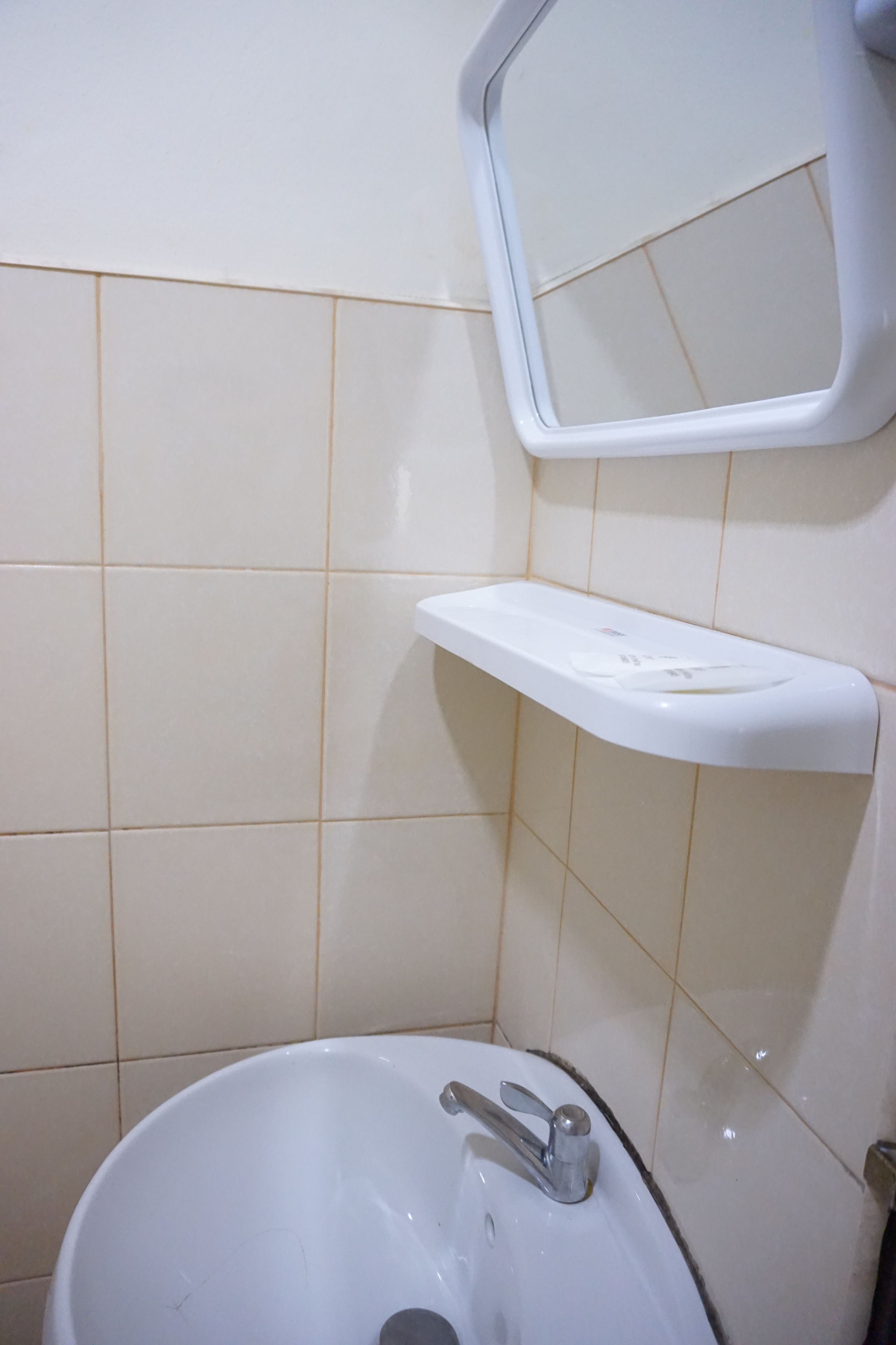 Un baño con un lavamanos blanco, un espejo y un estante sobre el lavamanos.