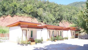 Una hilera de edificios pequeños de un solo piso, con un estilo arquitectónico uniforme, cada uno con puerta y ventanas, rodeado de una zona pavimentada con plantas en macetas.