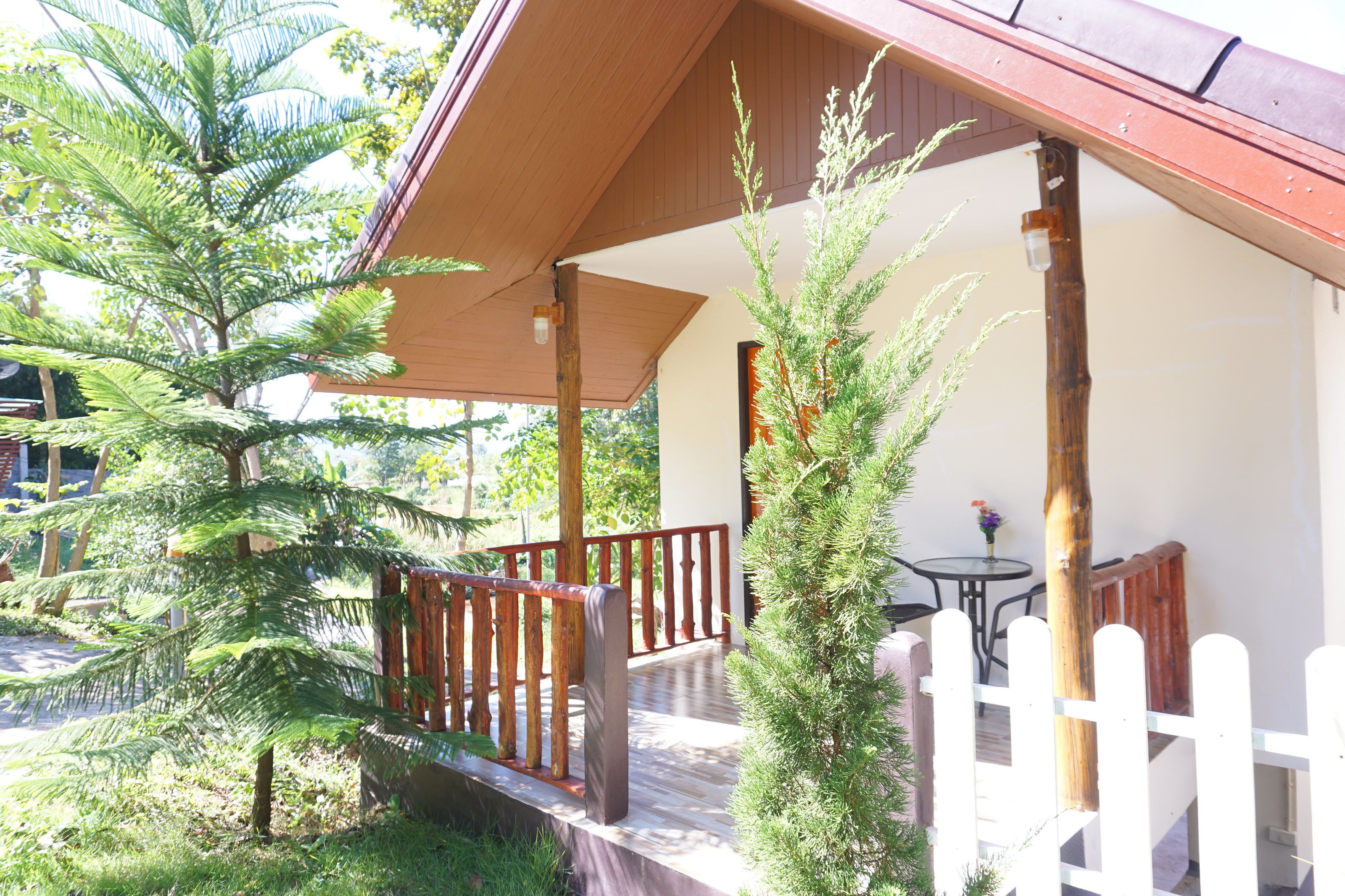 A covered outdoor area with a wooden deck, a white picket fence, and a small table with a vase of flowers.