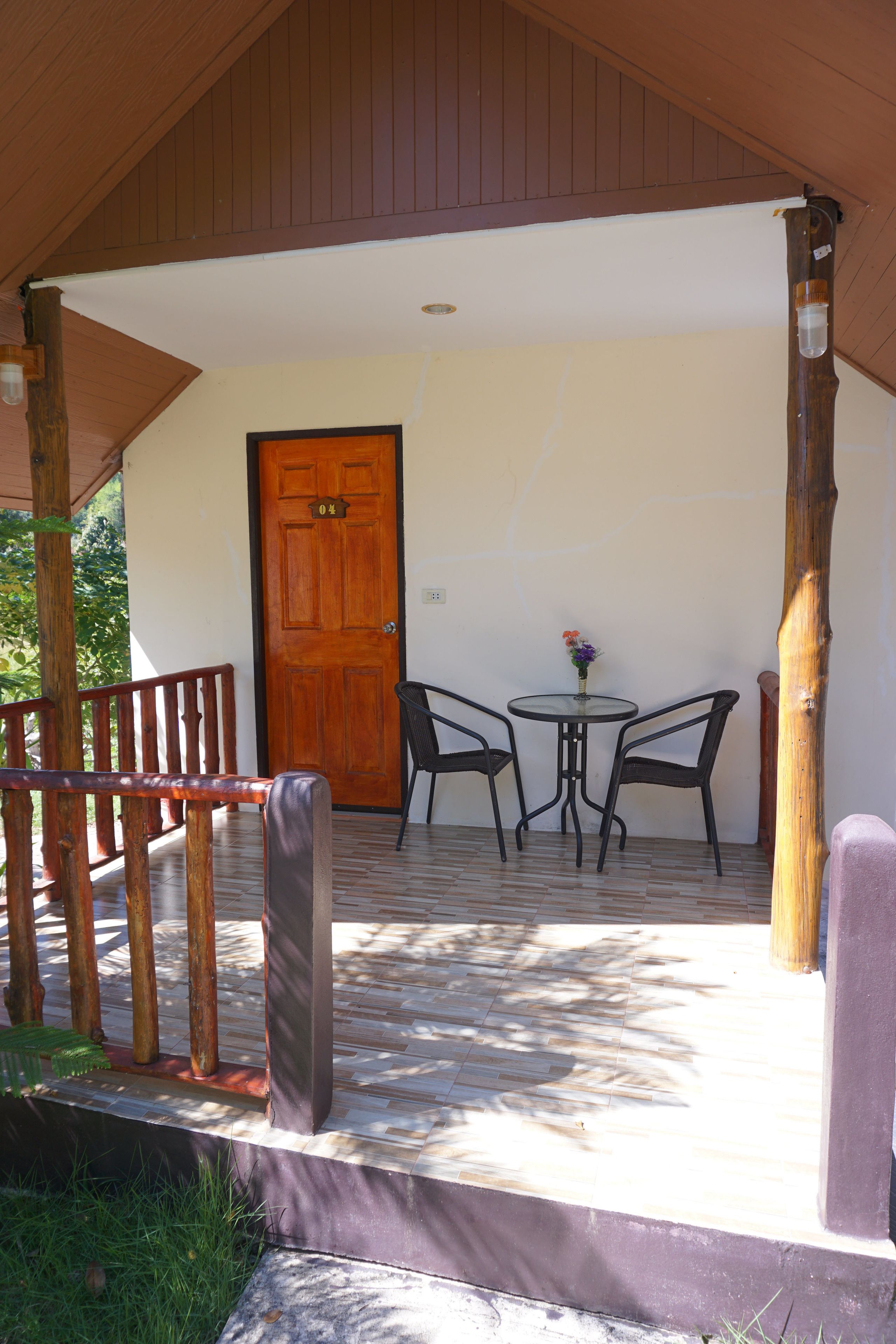 A wooden porch with a door, two chairs, and a small table with a vase of flowers.