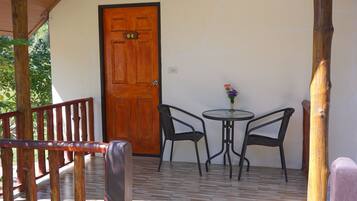 A wooden porch with a door, two chairs, and a small table with a vase of flowers.