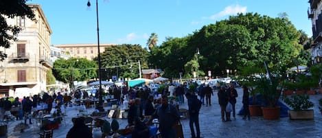 Μια υπαίθρια αγορά με τραπέζια και καρέκλες, που περιβάλλεται από κτίρια και δέντρα.