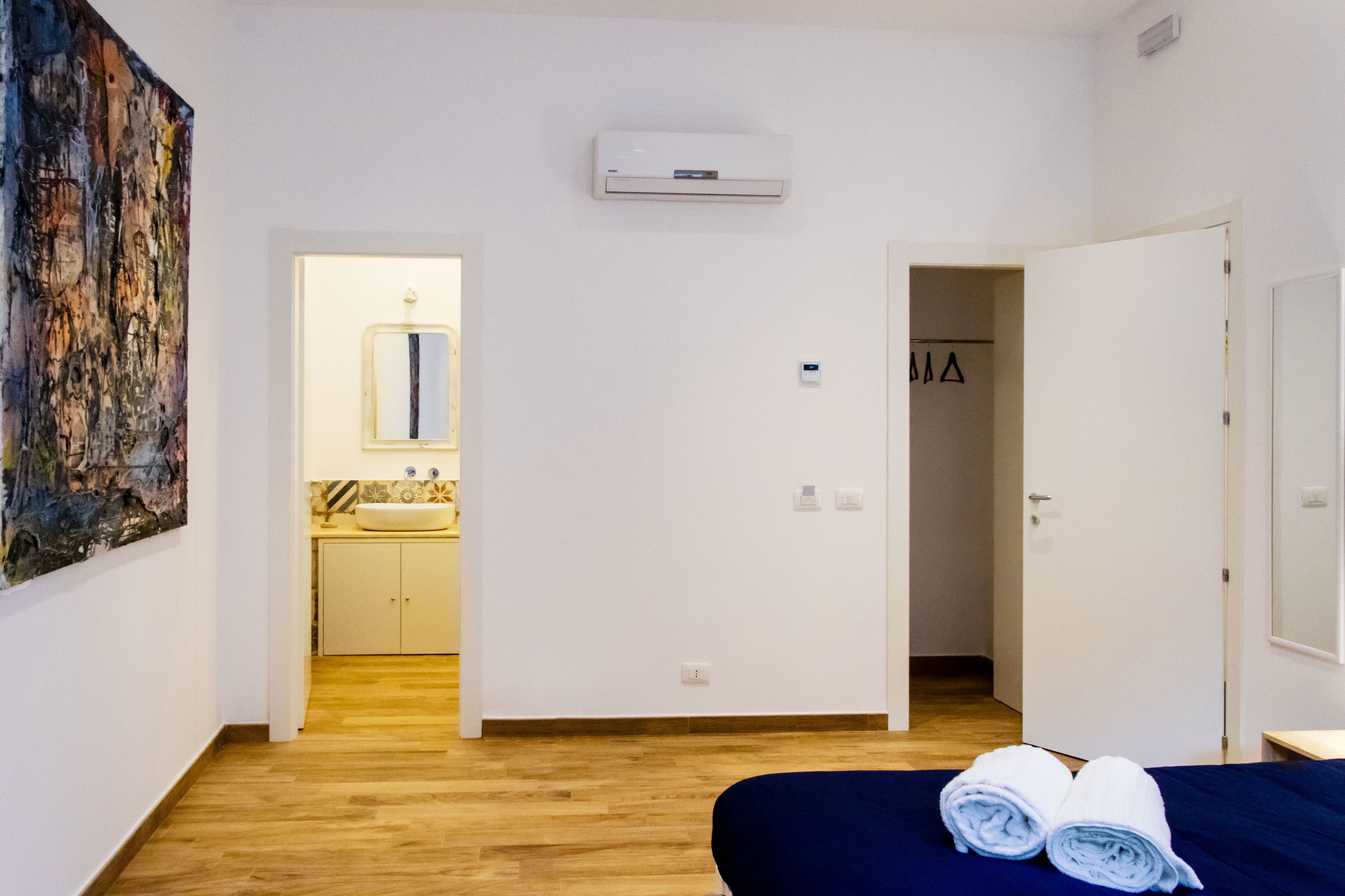 A hotel room with a bed, a bathroom with a sink, and a hallway leading to another room.