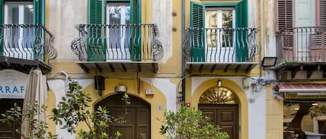 A building with a yellow facade, green shutters, and a sign for a wine and restaurant.
