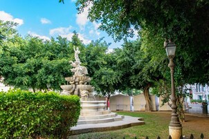 Una fuente de piedra de varios niveles y con estatuas, rodeada de abundante follaje y un farol.