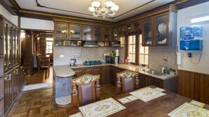 A spacious kitchen with wooden cabinets, a granite countertop, and a dining area with a large table and chairs. - Tokha Holiday Home (Tohka)