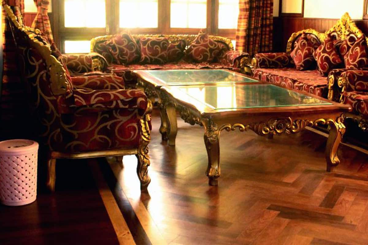 A traditional room with ornate furniture, a glass-top coffee table, and a patterned rug.