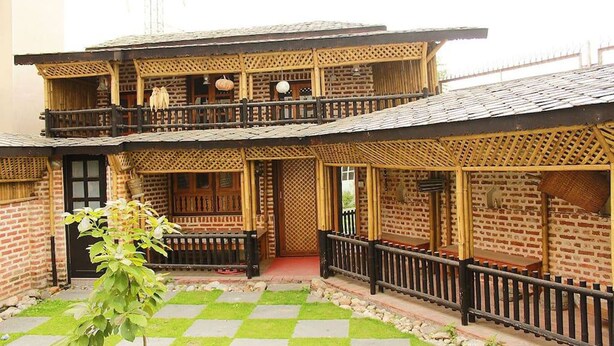 A two-story building with a balcony, a checkered lawn, and a small tree in the foreground. - Tokha Holiday Home (Tohka)