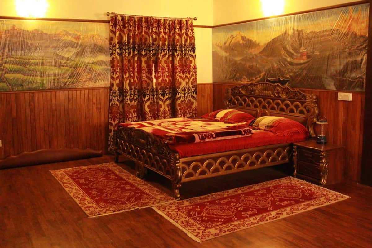 A traditional room with a wooden bed, two red and white patterned rugs, a wooden nightstand, and a large landscape painting on the wall.