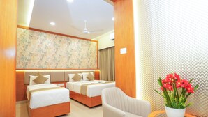 A hotel room with two beds, a sitting area with a chair, a small table with a vase of flowers, and a ceiling fan. - Zaith Residency, Chennai (Chennai)
