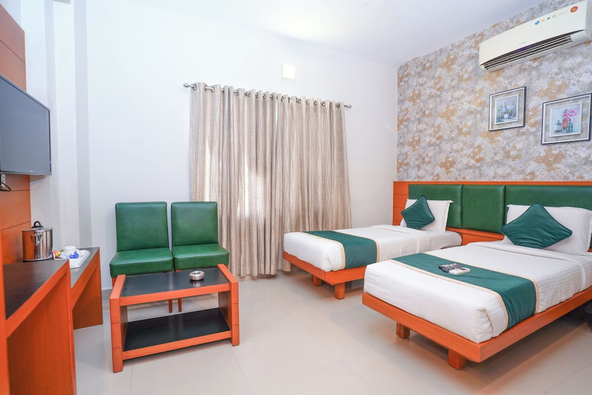 A hotel room with two single beds, a green sofa, a small table, and a TV.