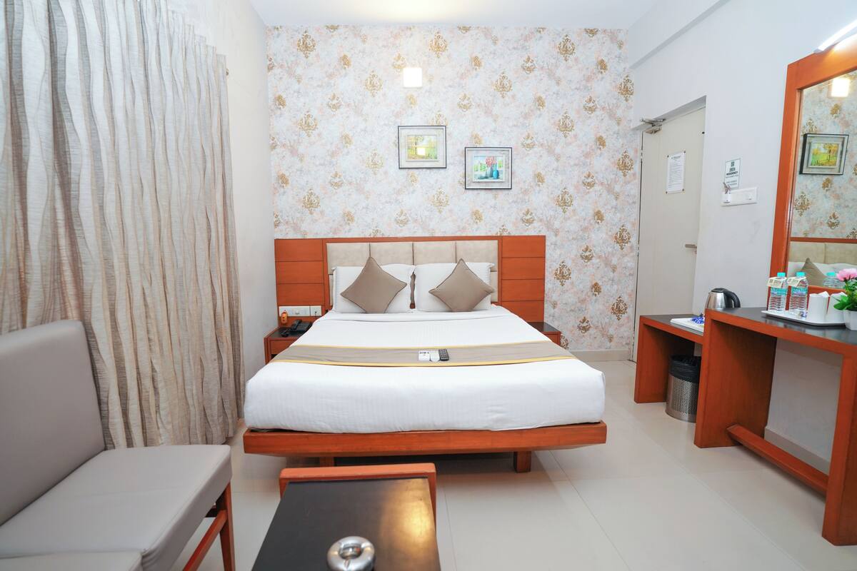 A hotel room with a bed, a desk, a chair, and a mirror.