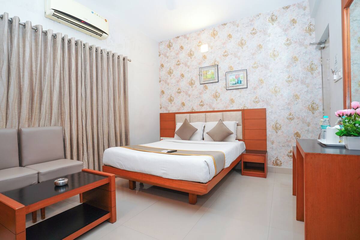 A hotel room with a bed, a sofa, a coffee table, a desk, and an air conditioner.