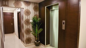 A hallway with a potted plant, an elevator, and patterned wallpaper. - Zaith Residency, Chennai (Chennai)