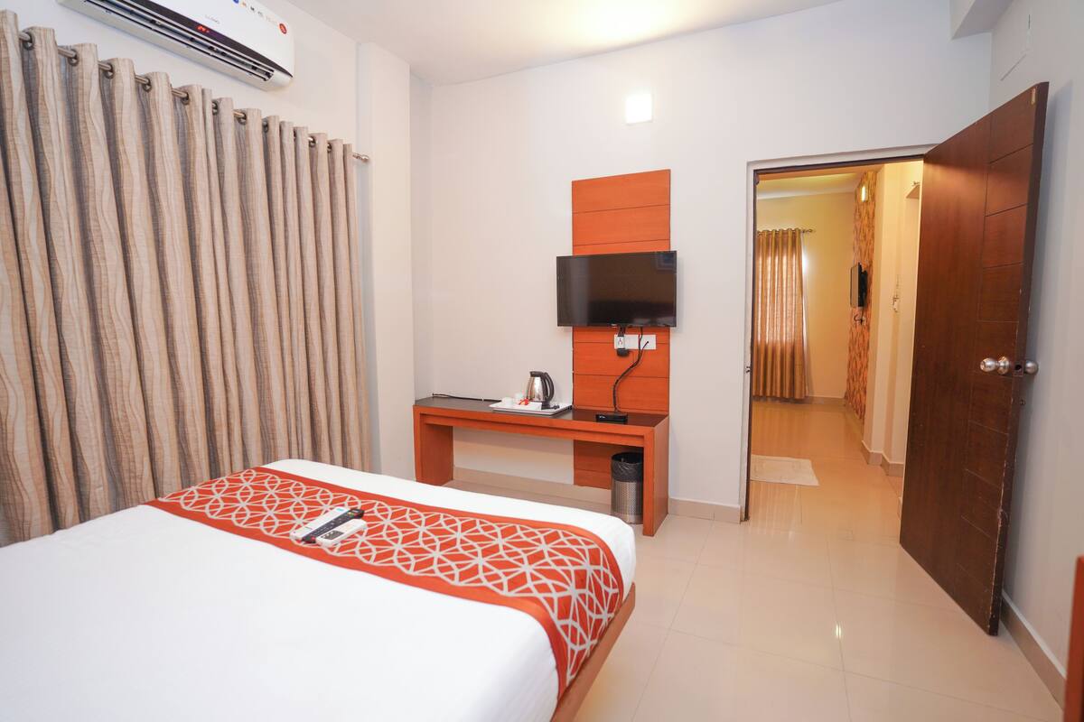 A hotel room with a bed, a desk with a flat-screen TV, a coffee maker, and a trash can.