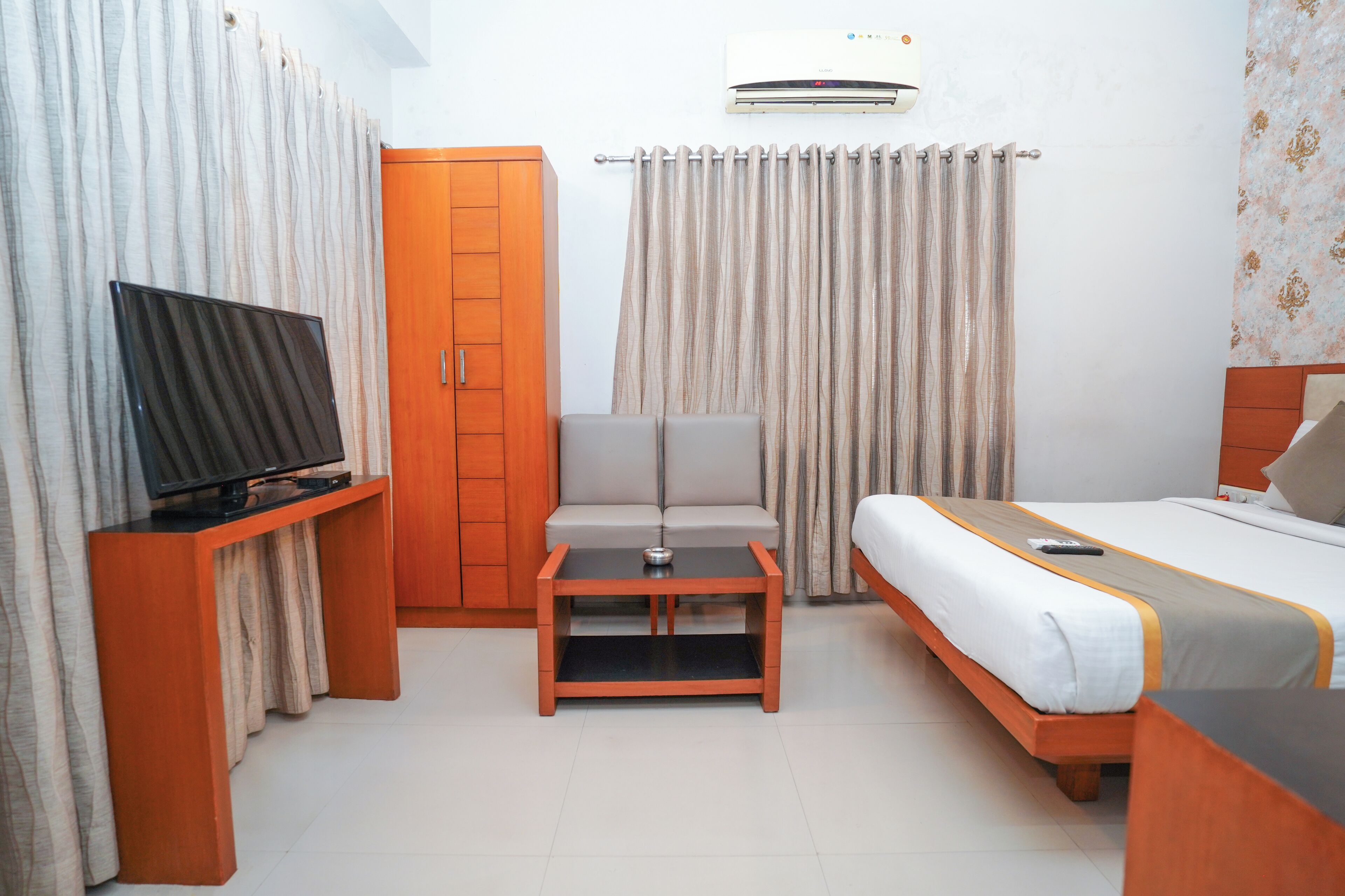 Una habitación de hotel con cama, televisor en un mueble, sofá y una mesita.