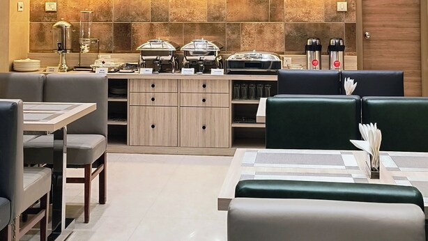 A modern dining area with a high ceiling, a ceiling fan, and a stone-tiled wall. There are dining tables and chairs, and a buffet counter with food items. - Zaith Residency, Chennai (Chennai)