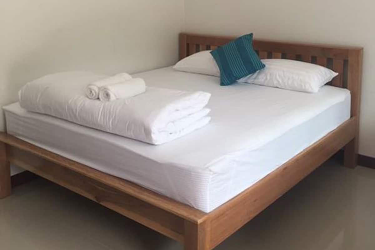 A neatly made bed with white linens and a rolled towel, a wooden headboard, and a wall-mounted air conditioner.