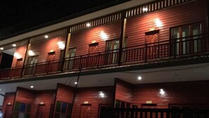 Ein zweistöckiges Gebäude mit Holzfassade, mehreren Balkonen und erleuchteten Fenstern.