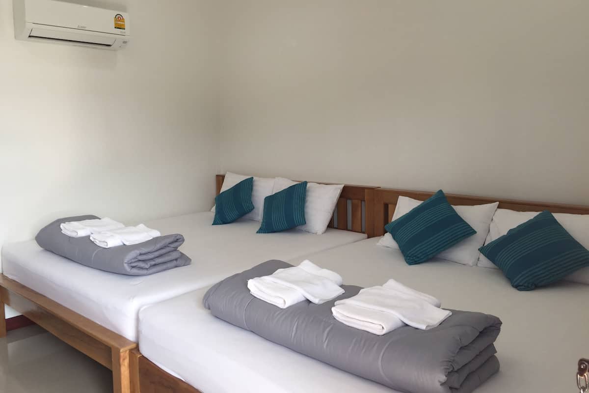 A double bed with grey and white bedding, teal pillows, and folded towels.