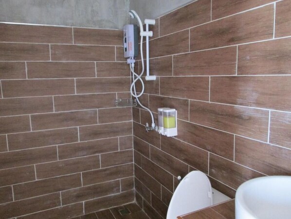 Un baño con paredes de azulejos marrones, un inodoro blanco y una zona de ducha con cabezal de ducha manual y dispensador de jabón.