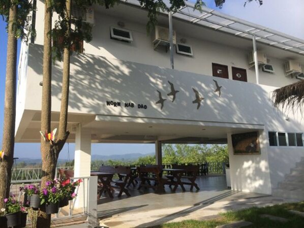 A building with a covered outdoor seating area, a sign with bird silhouettes, and hanging flower pots.
