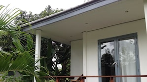 Una casa moderna con porche cubierto, amplios ventanales correderas y abundante vegetación alrededor.