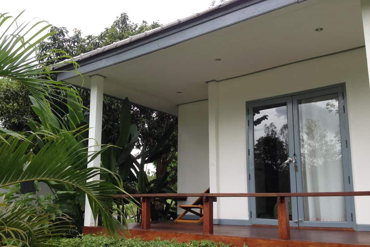 Una casa moderna con porche cubierto, amplios ventanales correderas y abundante vegetación alrededor.