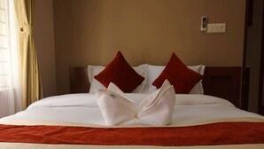 Una cama bien hecha con ropa blanca y dos almohadas rojas, una manta roja y un cabecero de madera.