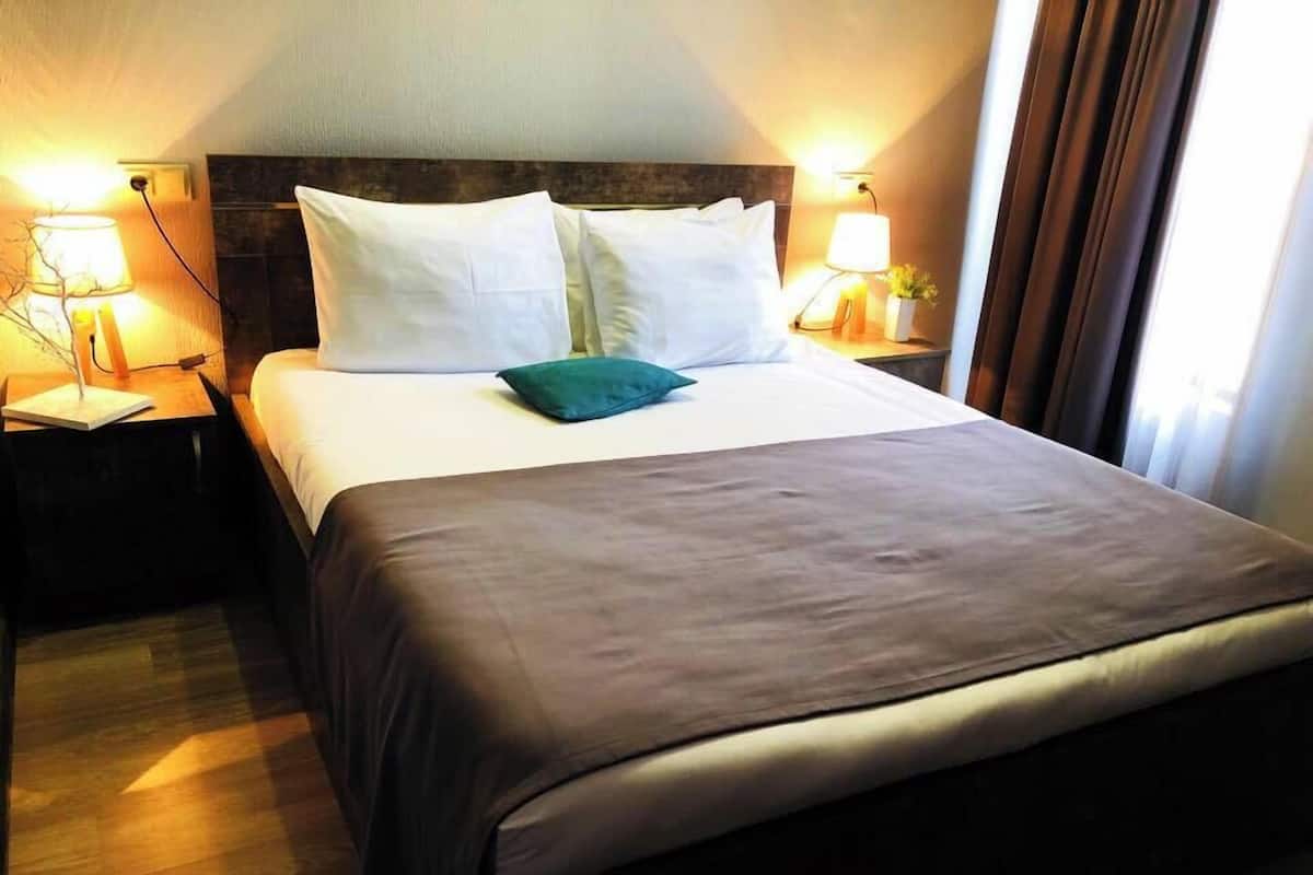A hotel room with a large bed, two bedside lamps, and a nightstand with a lamp.