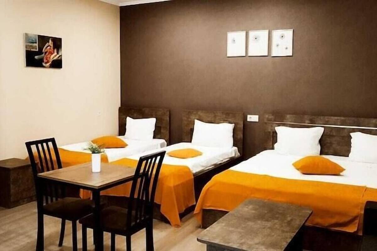 A hotel room with two beds, a desk, chairs, a wardrobe, and artwork on the wall.