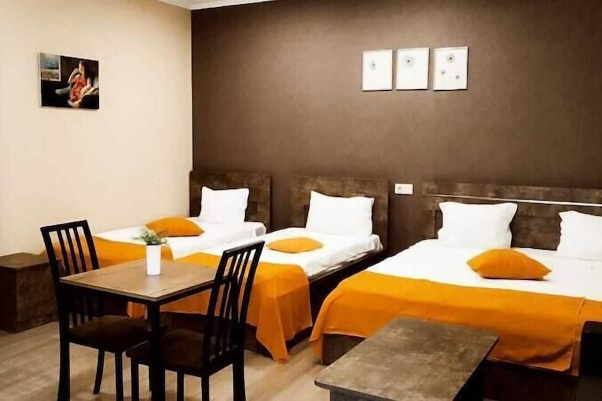 A hotel room with two beds, a desk, chairs, a wardrobe, and artwork on the wall.